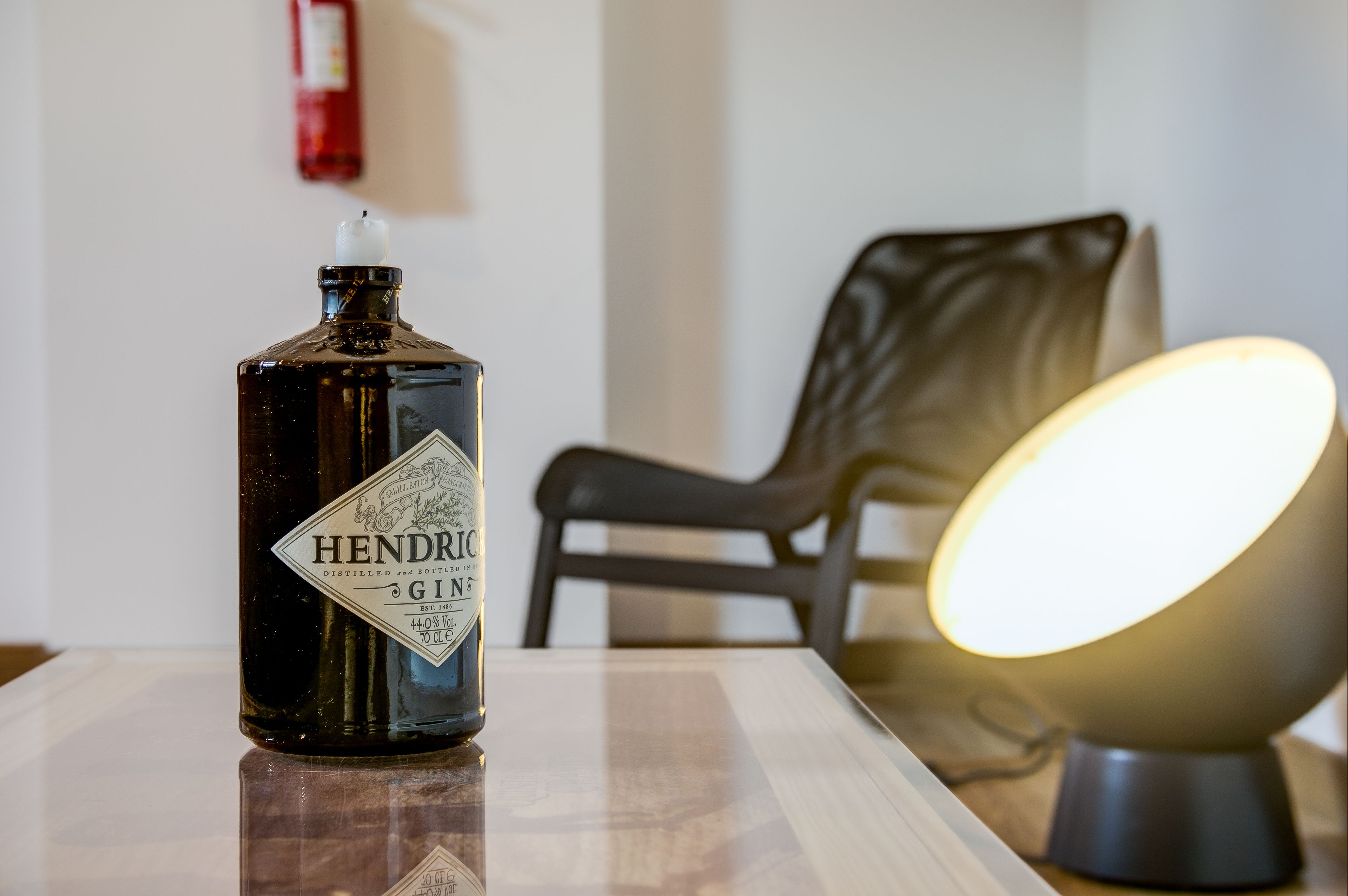 Une bouteille de gin Hendrick’s est posée sur une table, avec une chaise et une lampe en arrière-plan.