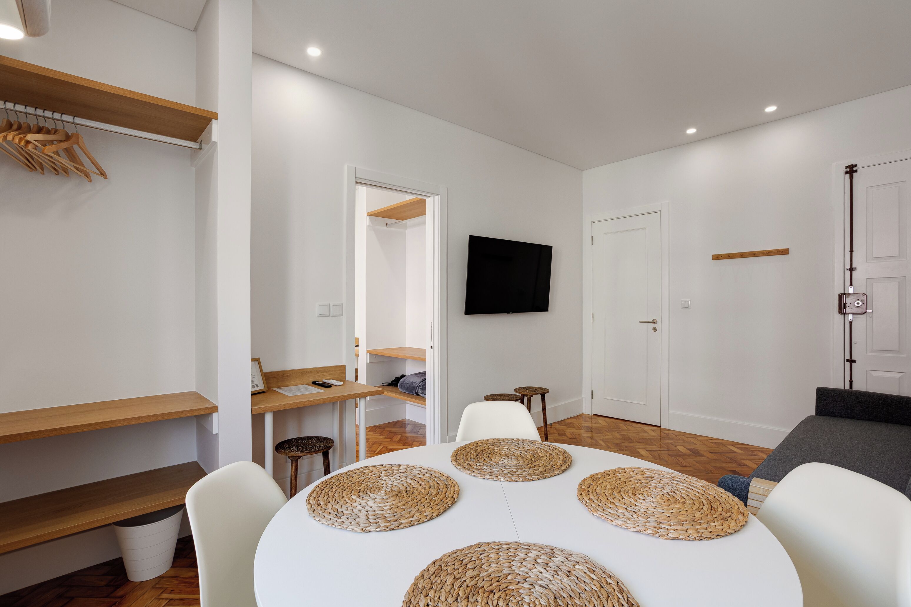 Una sala de estar moderna con una mesa de comedor, sillas blancas, un sofá, un televisor y una estantería de madera.