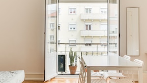 Een balkon met een tafel en stoelen, een bloempot en uitzicht op omliggende gebouwen.