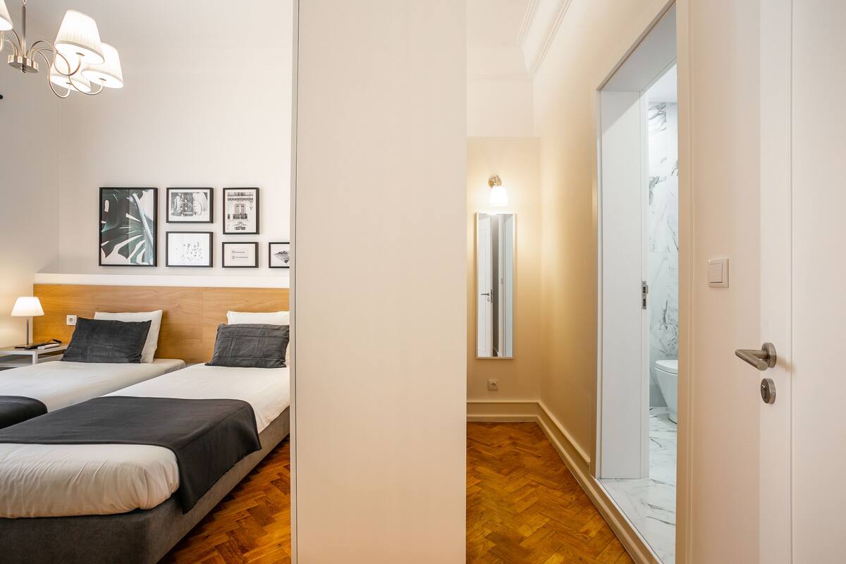 Une chambre d’hôtel avec deux lits, un plancher en bois, un mur orné de tableaux encadrés, une table de chevet et une lampe.