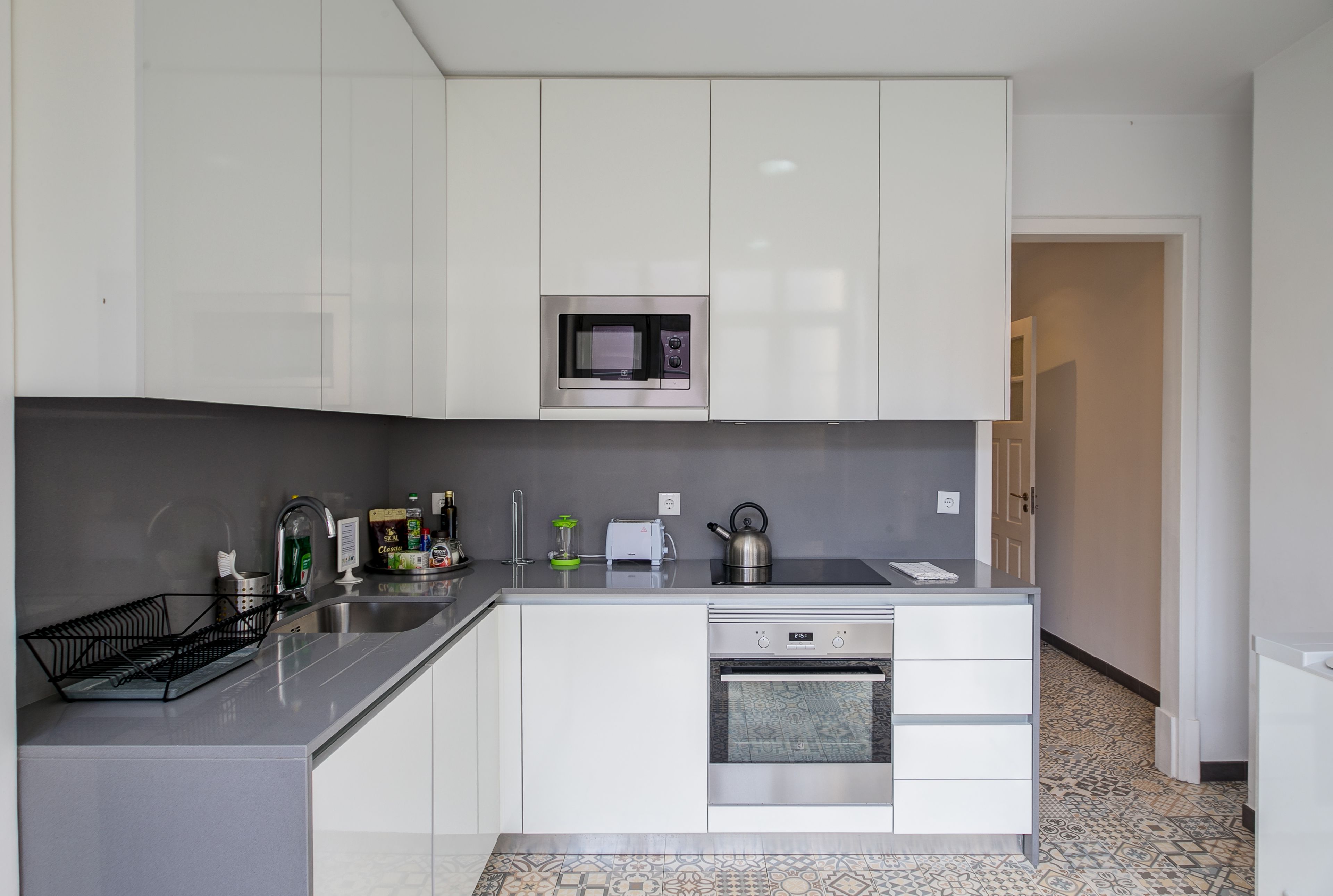 Una cocina moderna con armarios blancos, microondas integrado, hervidor y tostadora.