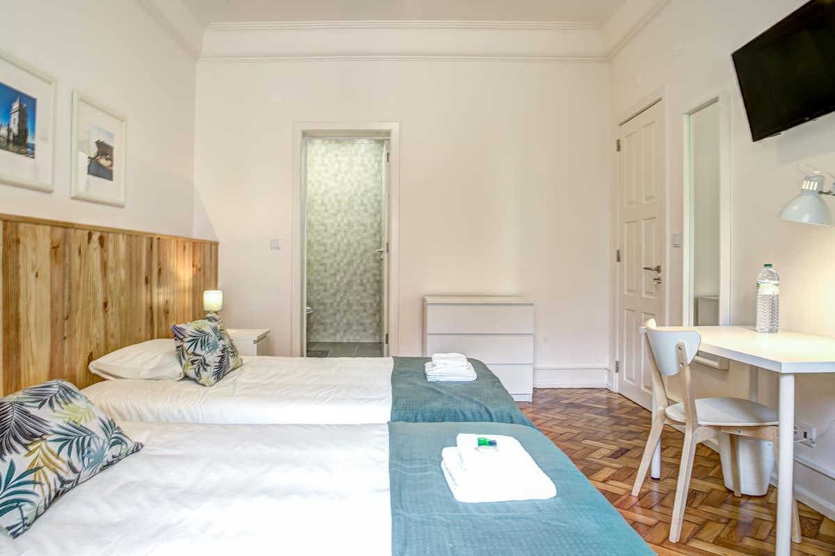 Une chambre d’hôtel avec deux lits, un bureau, une chaise, une télévision et une douche.