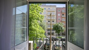 Uitzicht vanaf een balkon met een metalen hekwerk, uitkijkend op een parkeerplaats met verschillende auto's en een gebouw met veel ramen op de achtergrond.