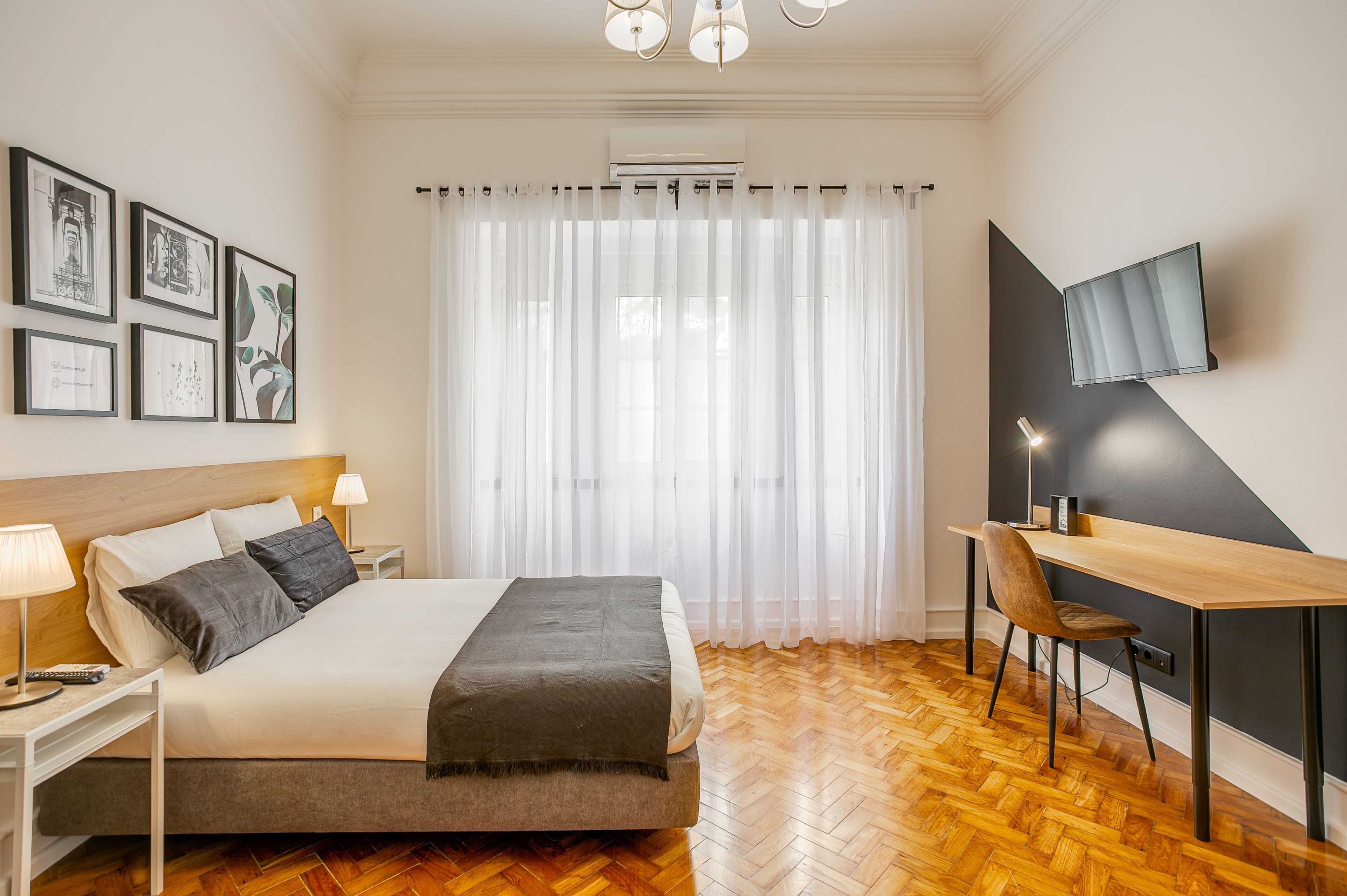 A bedroom with a bed, bedside tables, a desk, a chair, a TV, and a window with curtains.