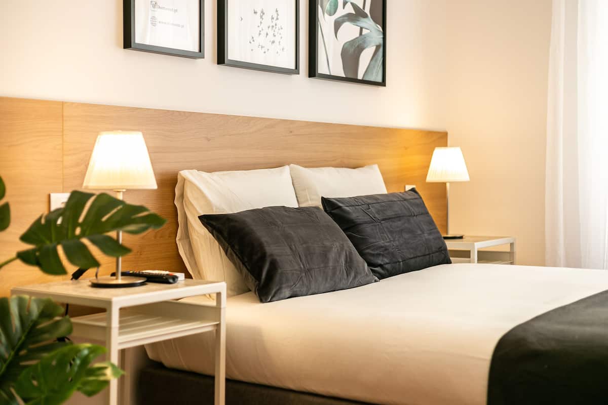 Un lit bien fait, avec une tête de lit en bois, deux tables de chevet avec des lampes et des œuvres d’art encadrées accrochées au mur.