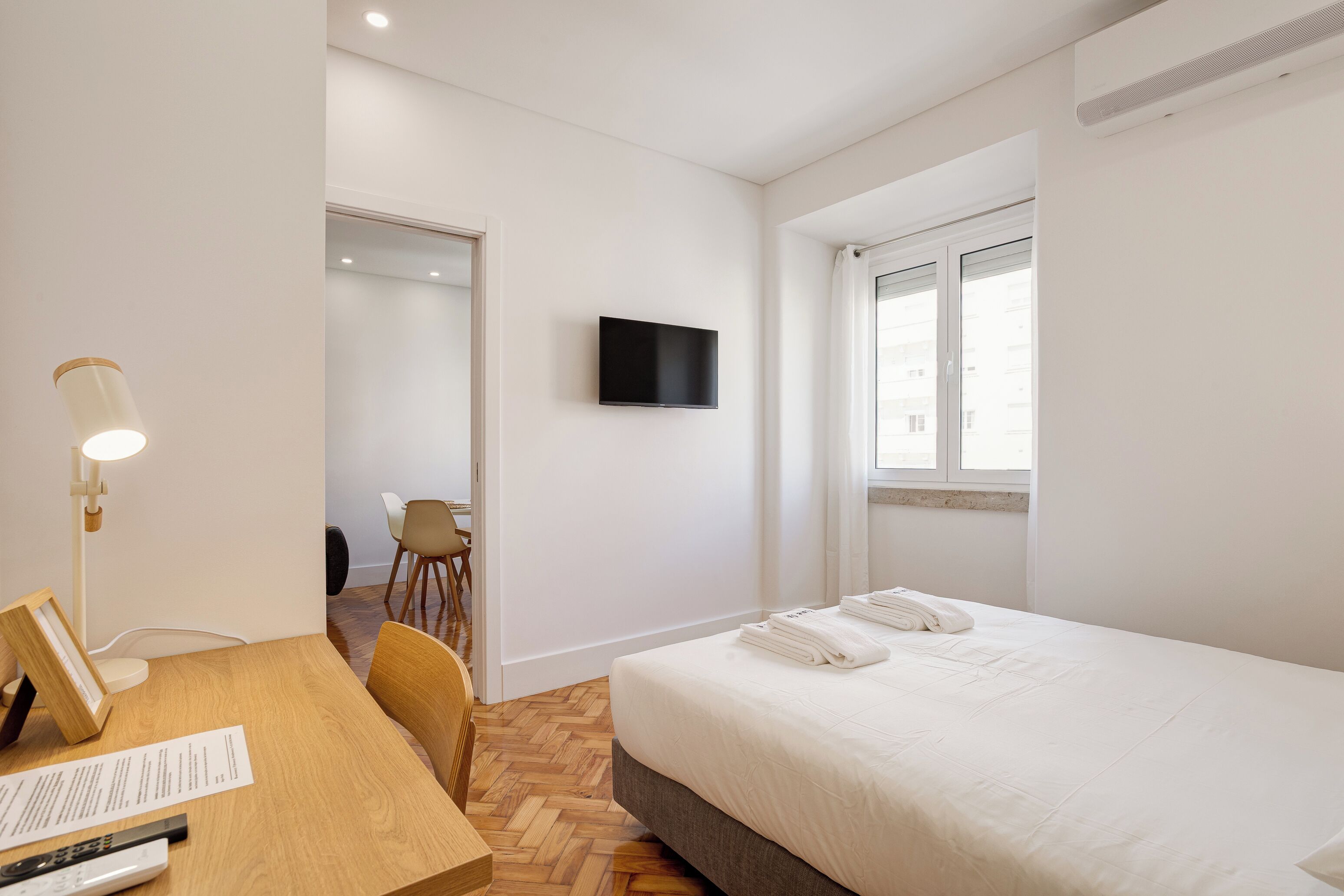 Habitación de hotel con cama, escritorio con lámpara, televisor en la pared y ventana.