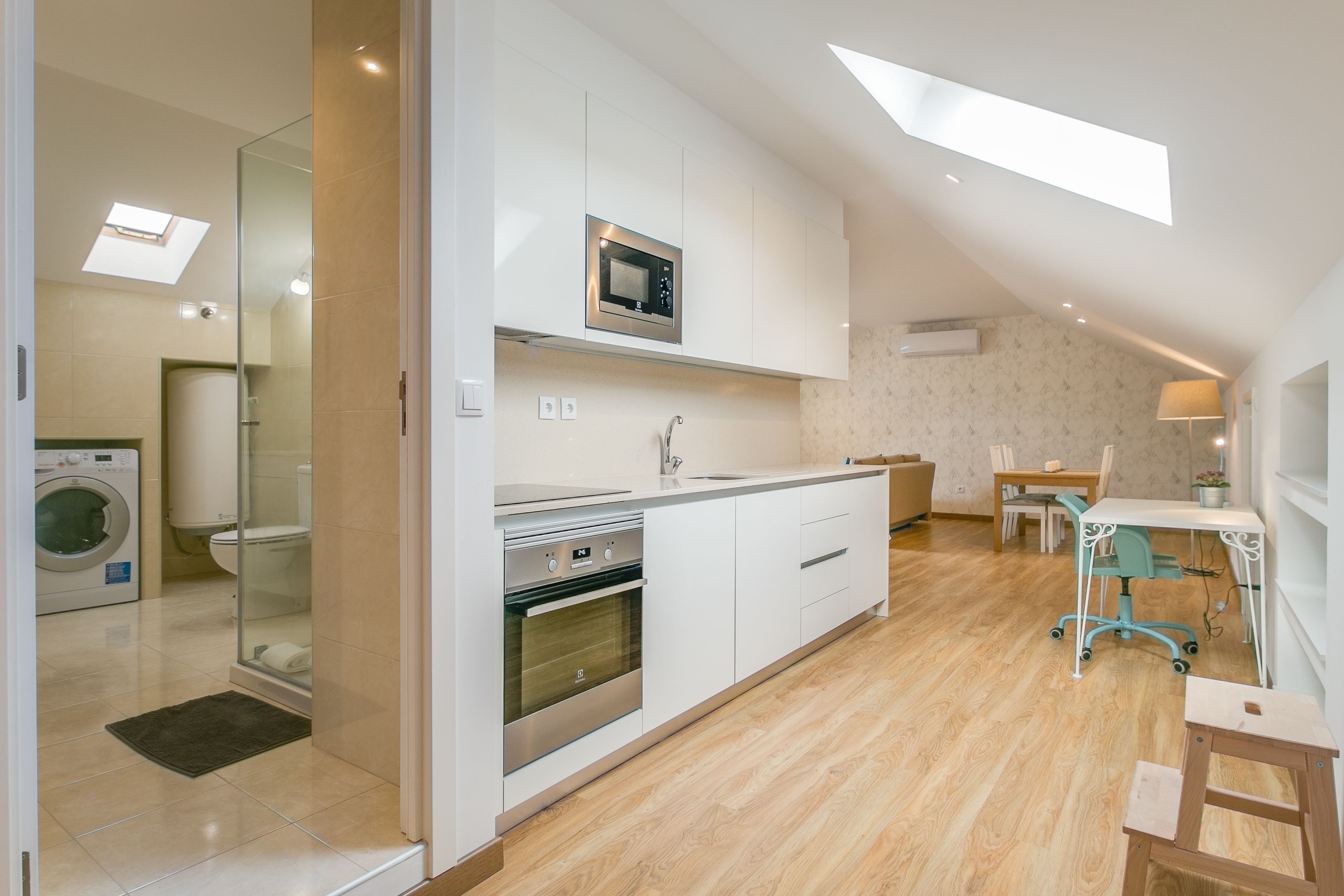 A modern kitchen with a built-in microwave, oven, and sink. There is a dining area with a table and chairs, and a small workspace with a chair and desk.