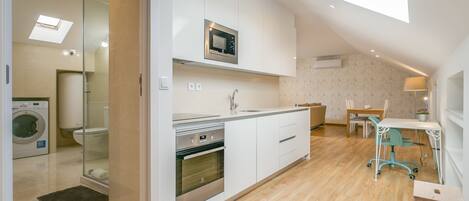 A modern kitchen with a built-in microwave, oven, and sink. There is a dining area with a table and chairs, and a small workspace with a chair and desk.