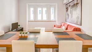 Een moderne woonkamer met een houten eettafel, witte banken en een groot abstract schilderij aan de muur.