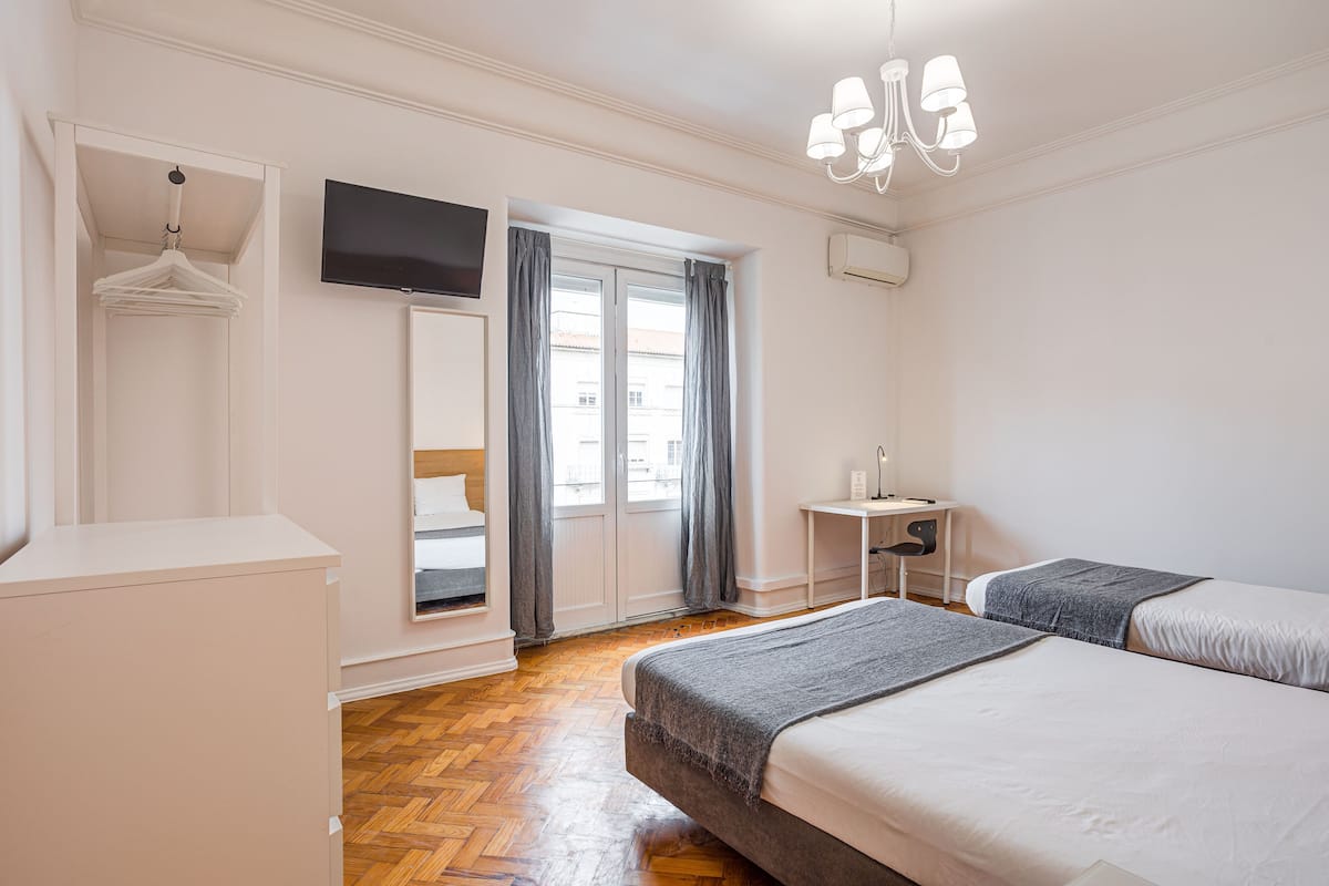 Une chambre avec deux lits, un bureau, une télévision et une armoire.
