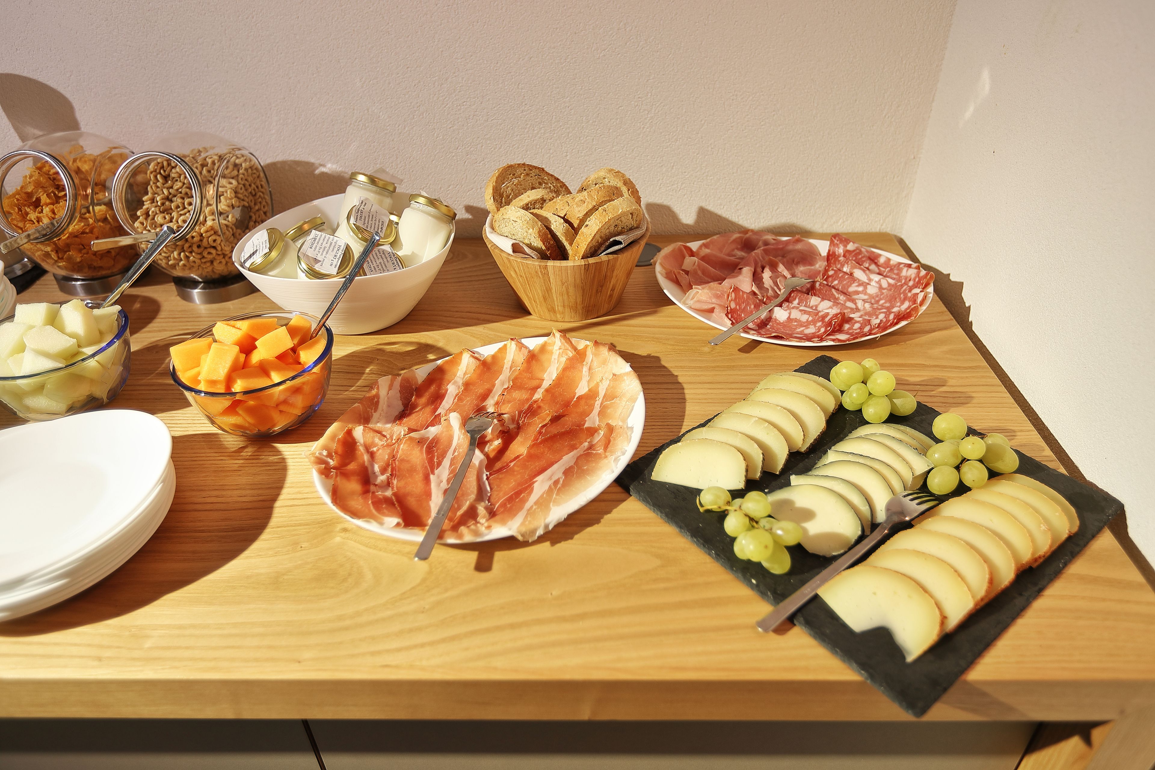 Un tavolo in legno con diversi cibi, tra cui formaggi, salumi e frutta.