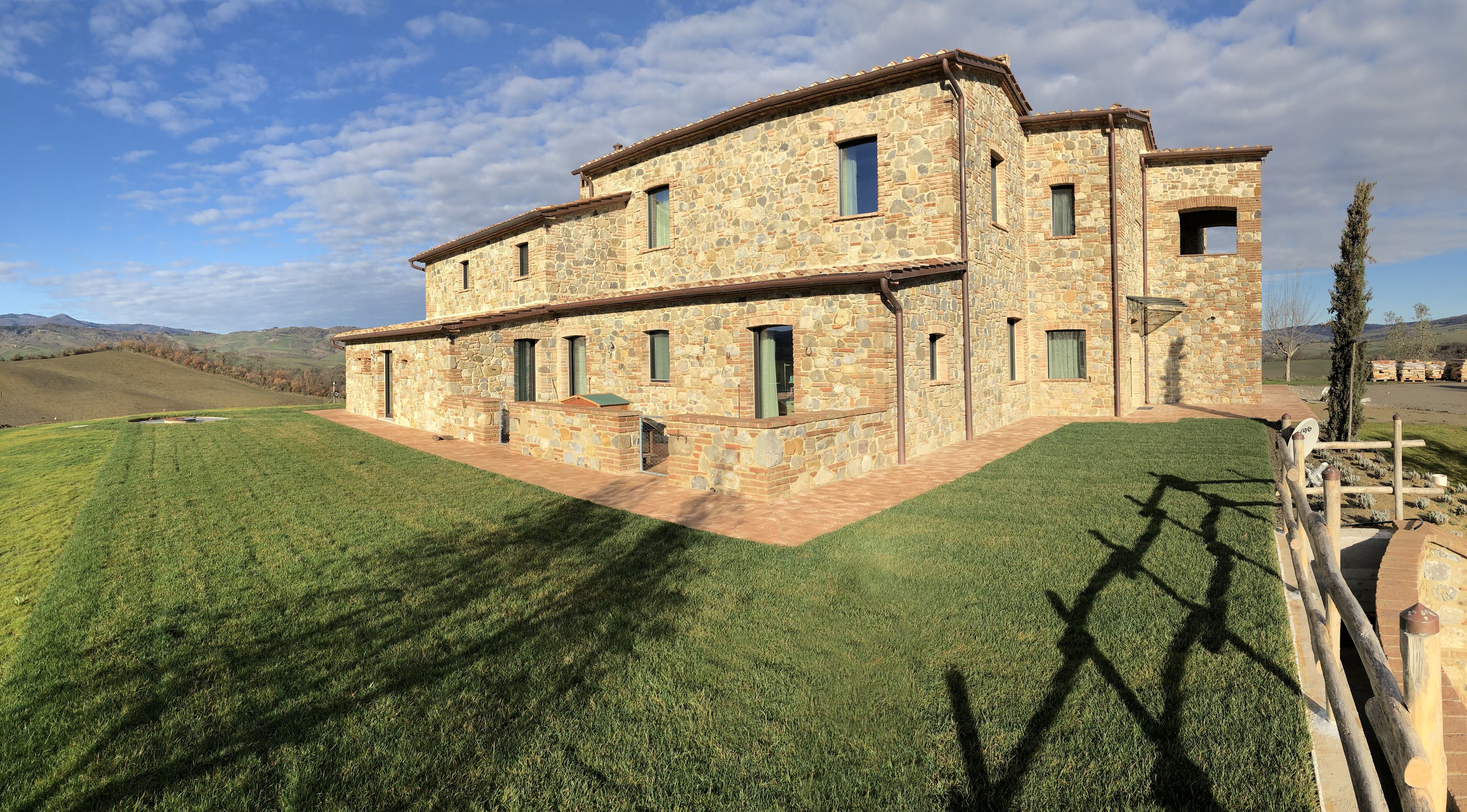 A stone building with multiple windows and a flat roof, surrounded by a well-maintained lawn and a hilly landscape in the background.