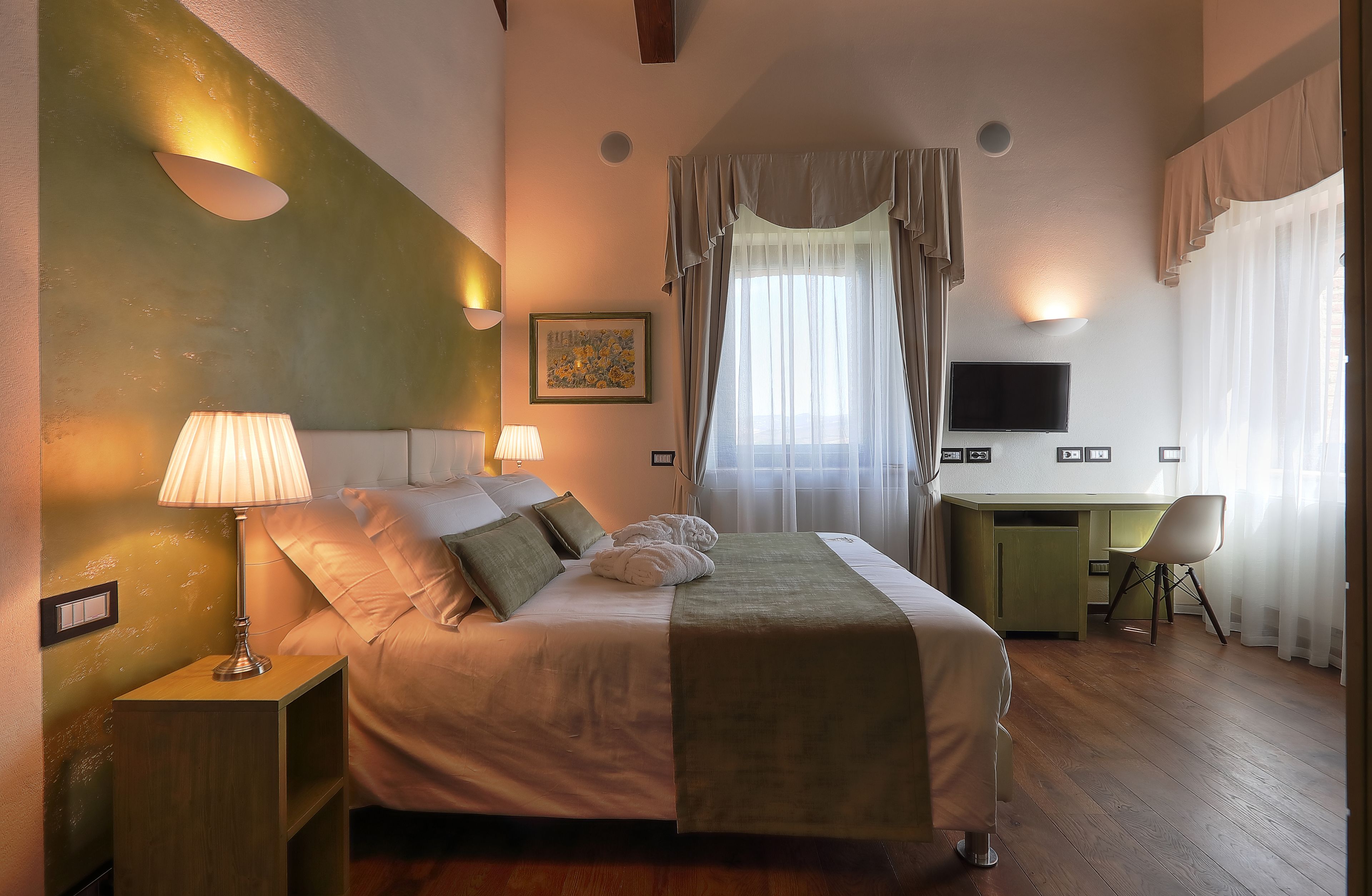 Une chambre à coucher comprenant un lit, des lampes de chevet, un bureau, une chaise, un téléviseur et une fenêtre avec des rideaux.