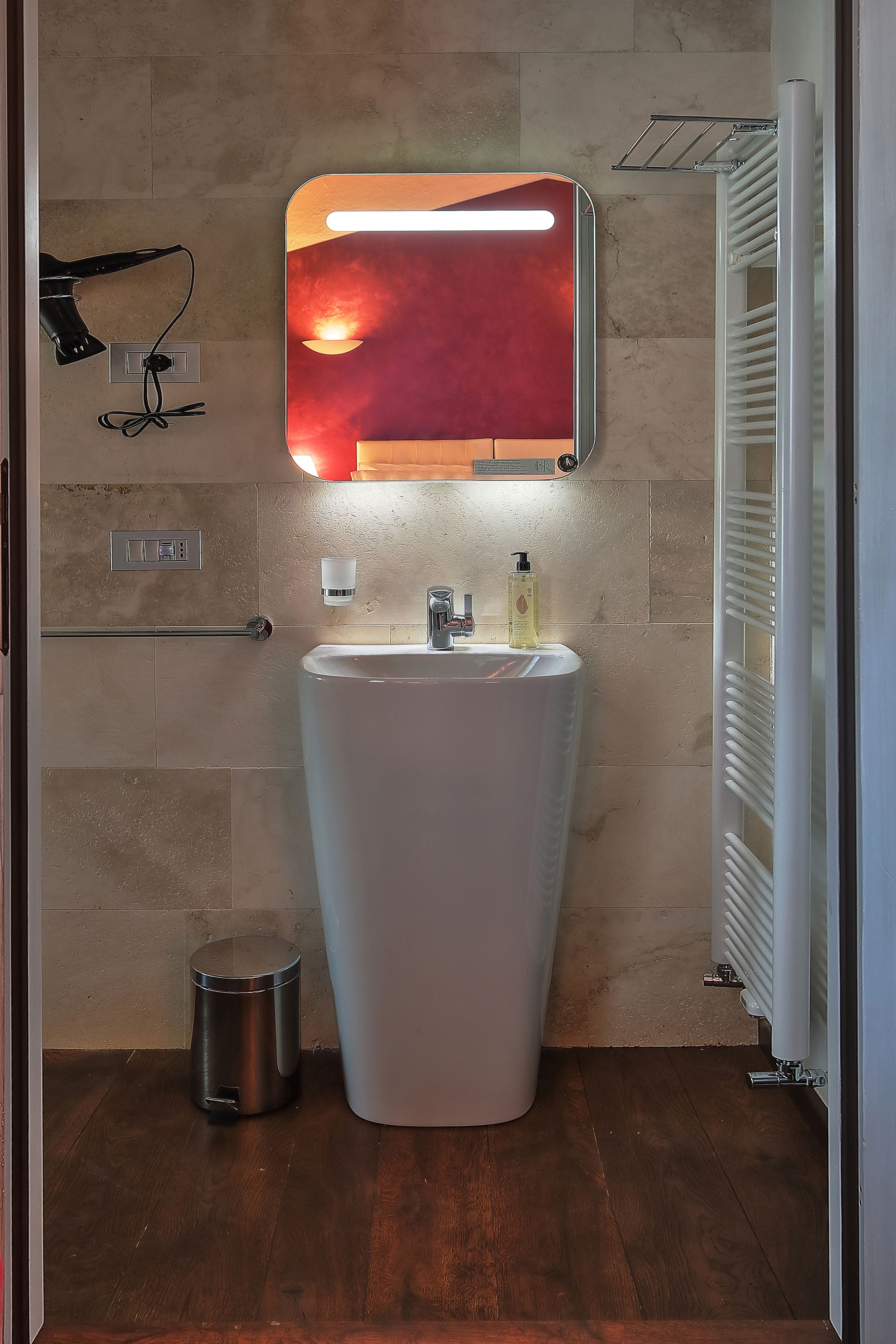 Un baño con un lavamanos grande de color blanco, un espejo, un secador de pelo y un cesto de basura.