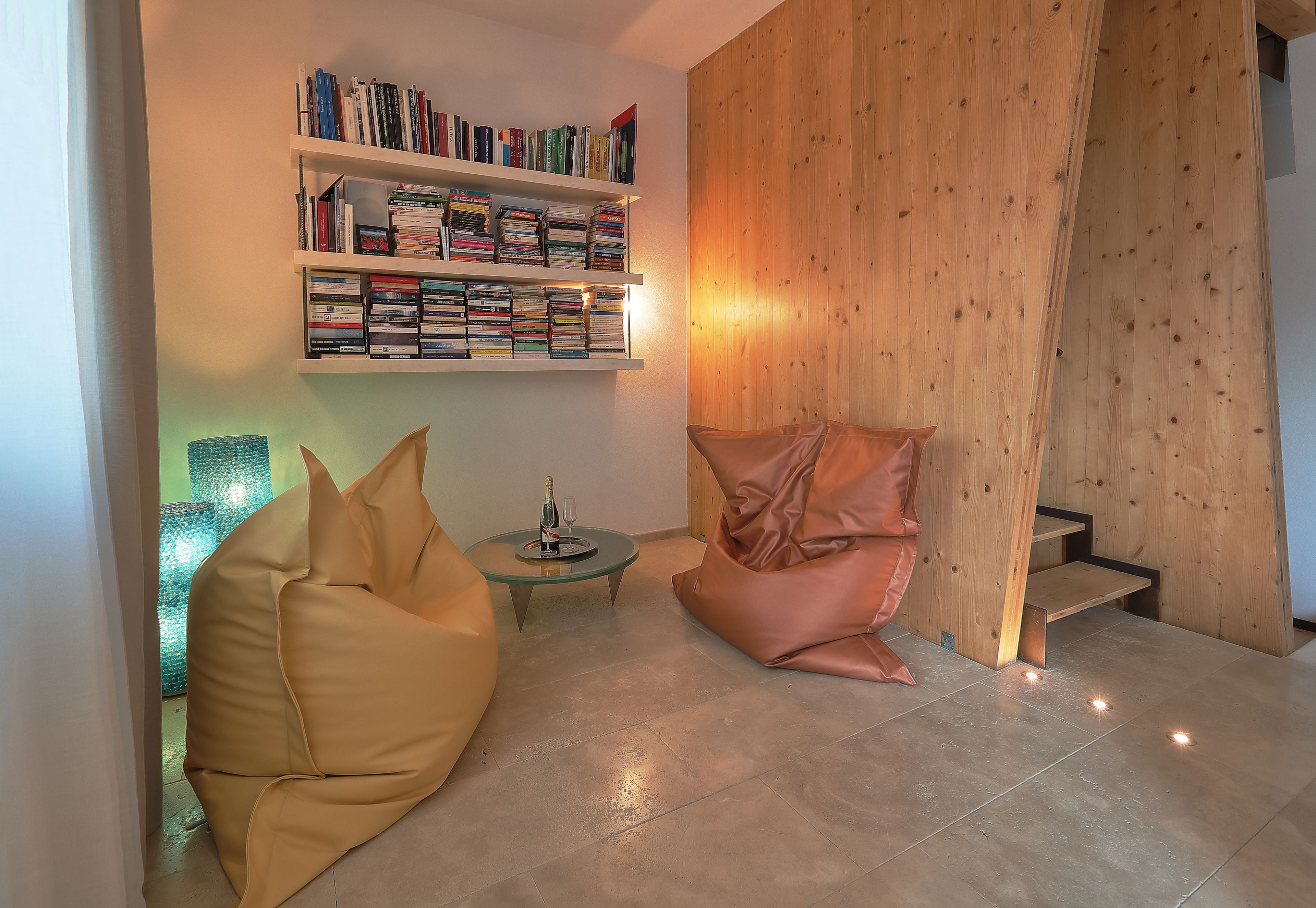 A modern living room with a bookshelf, a glass coffee table, a bean bag chair, and a wooden wall.