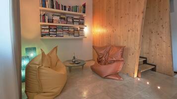 A modern living room with a bookshelf, a glass coffee table, a bean bag chair, and a wooden wall.