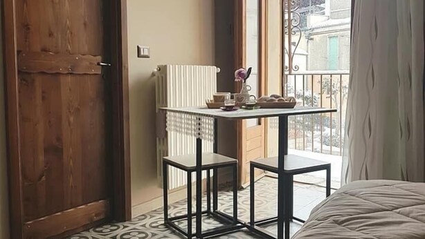 Un dormitorio con una cama grande, una mesita con dos sillas, un radiador y vistas al balcón exterior.