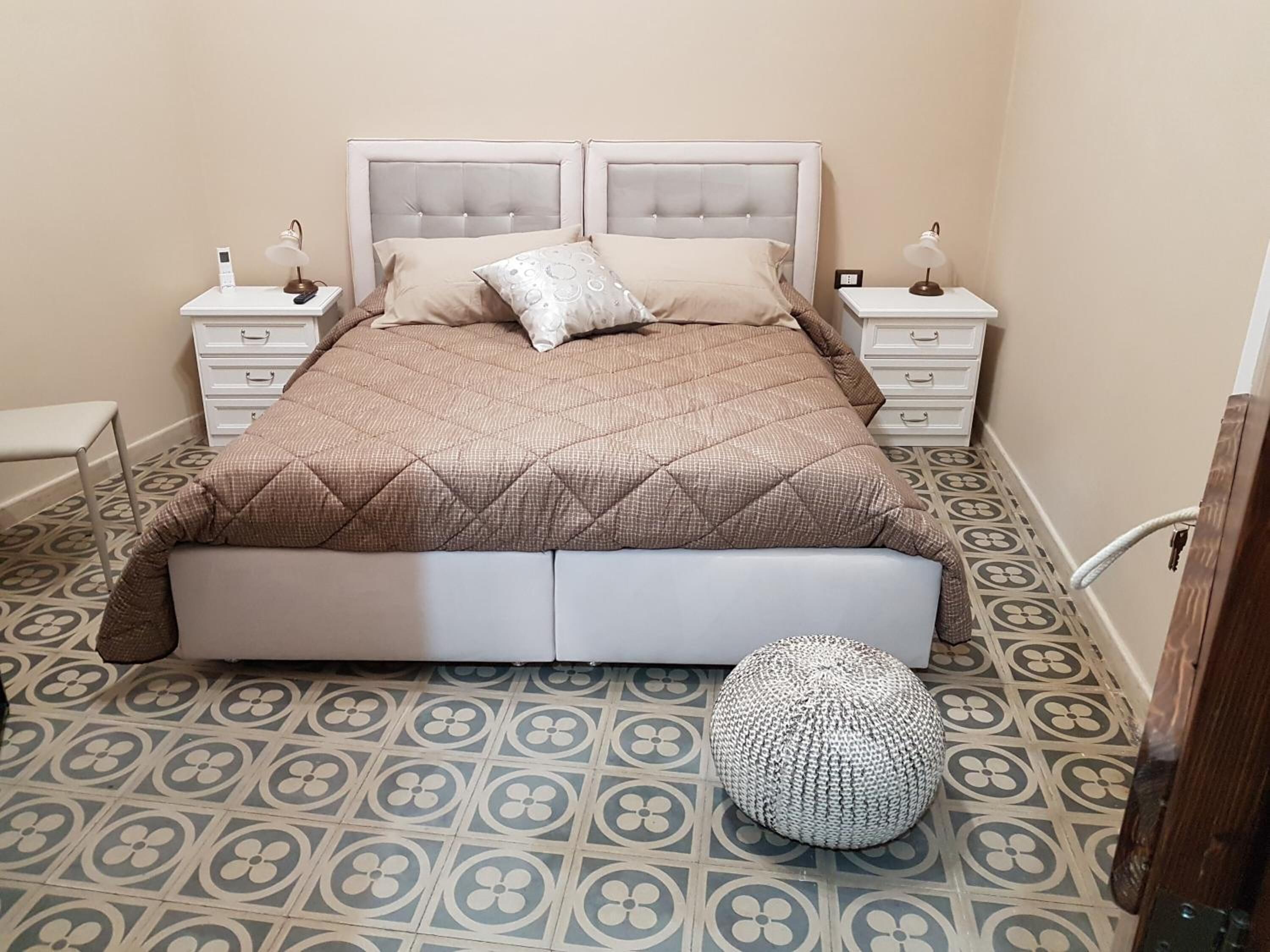 Une chambre à coucher comprenant un lit, deux tables de chevet, une commode, une chaise et un sol à motifs.