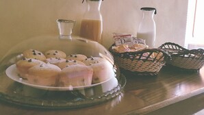 Una mesa para el desayuno con una bandeja cubierta de muffins, dos botellas de leche y una cesta de pan.
