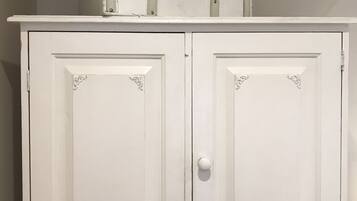 A white cabinet with two doors and a drawer, topped with stacked suitcases.