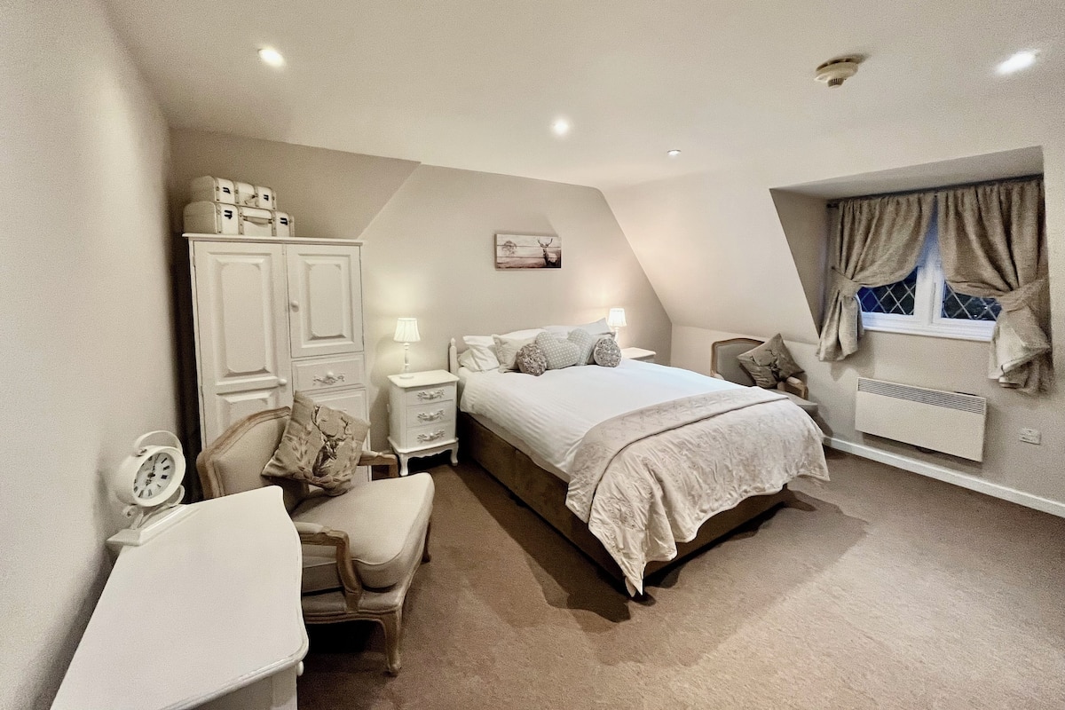 A bedroom with a bed, bedside tables, a chair, a desk, a wardrobe, and a window with curtains.