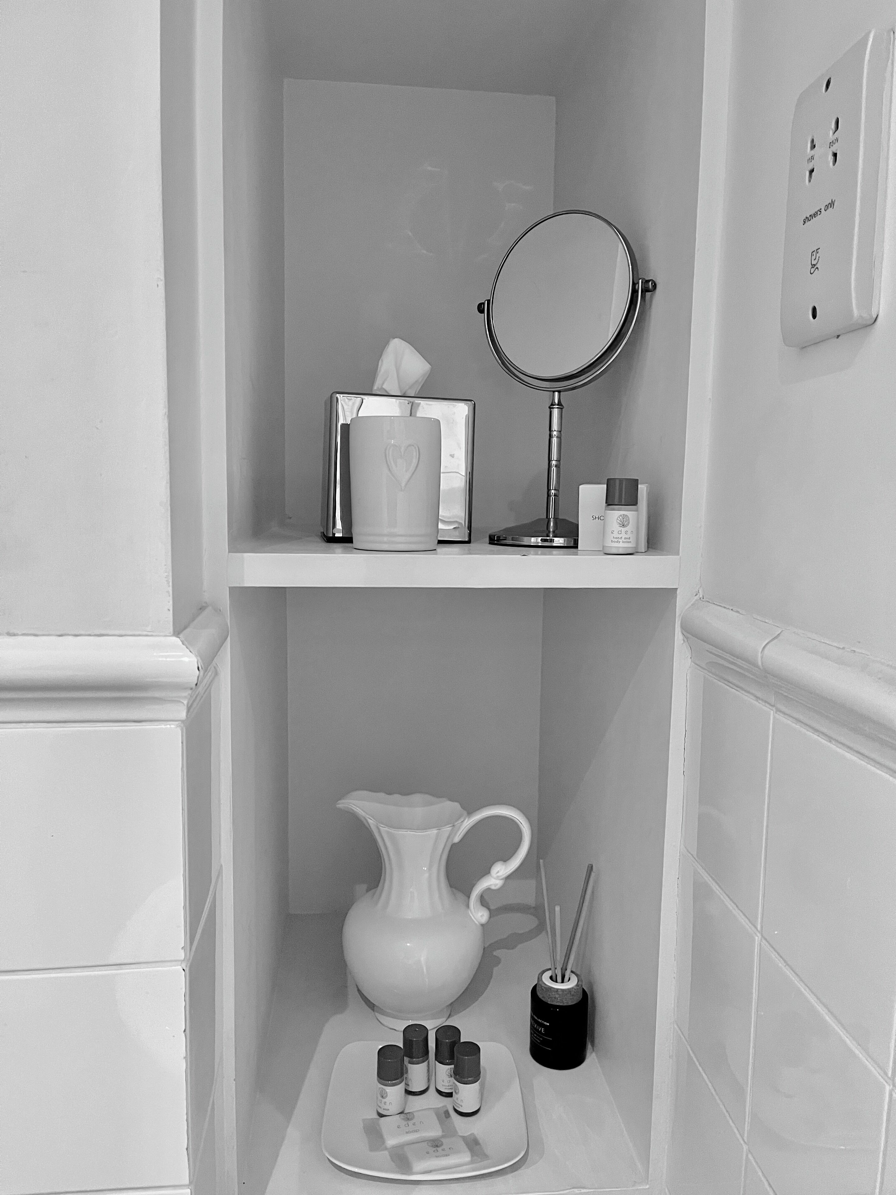 A bathroom with a mirror, a tissue box, a small bottle, a pitcher, and essential oils on a tray.