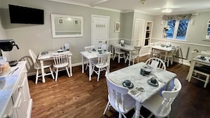 A dining area with white furniture, a flat-screen TV mounted on the wall, and a window with a view. - Park Farm Bed and Breakfast (Windsor)