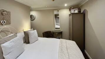 A hotel room with a bed, a chair, a small table, a wardrobe, and a mirror.