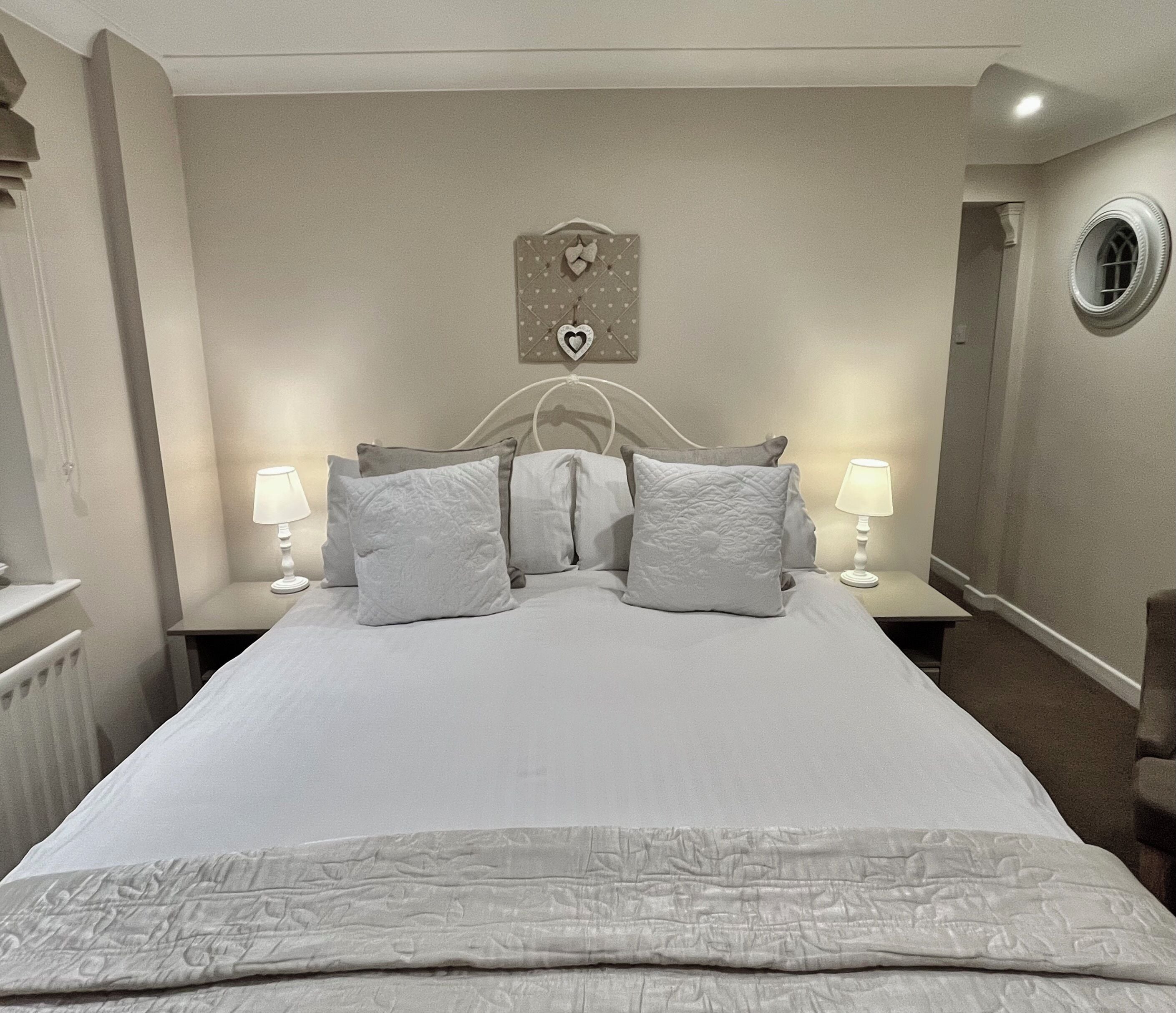 A neatly made bed with a white duvet and pillows, a bedside table with a lamp, and a wall clock.