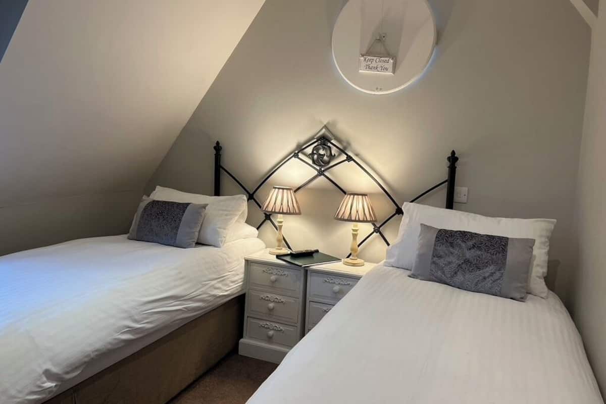 A bedroom with two single beds, a nightstand with lamps, and a ceiling light fixture.