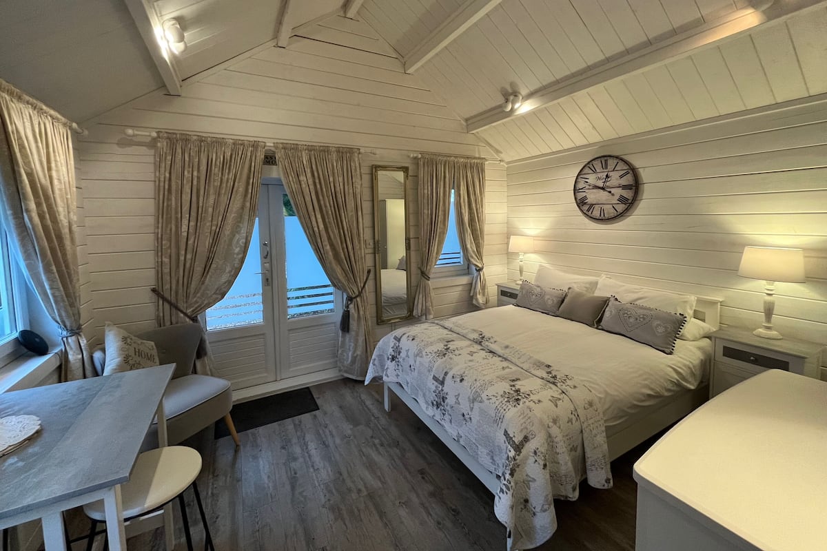 A cozy bedroom with a bed, bedside tables, a clock, and a window with curtains.