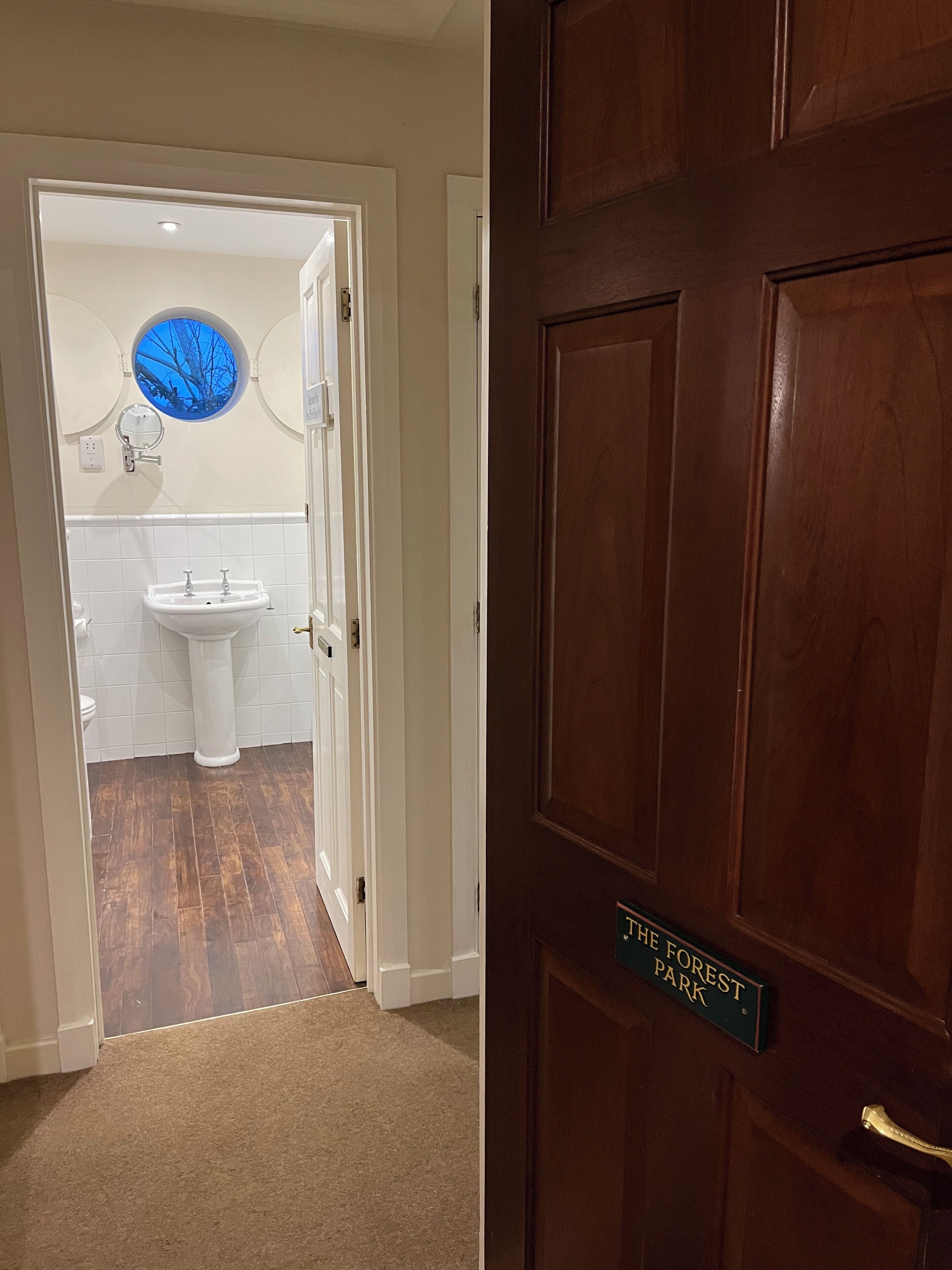 Un baño con lavamanos, inodoro y espejo con ventanal circular.