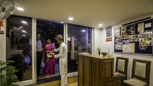 Zona de recepción con mostrador de madera, un tablón de anuncios con fotografías y puerta de vidrio de acceso.