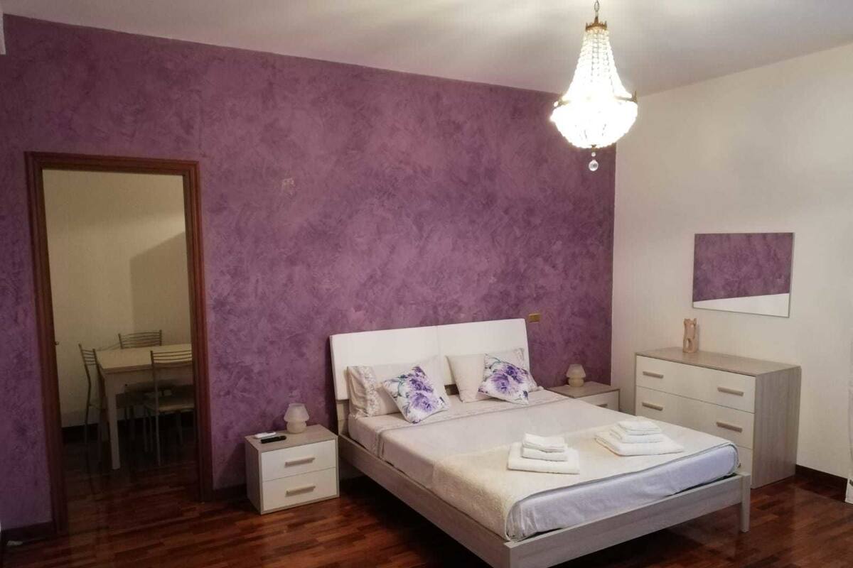 Une chambre à coucher comprenant un lit, des tables de chevet, une commode, un miroir et un lustre.