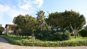 Un chemin pavé mène à un bâtiment doté d’un toit en tuiles, entouré d’une végétation luxuriante et d’arbres.