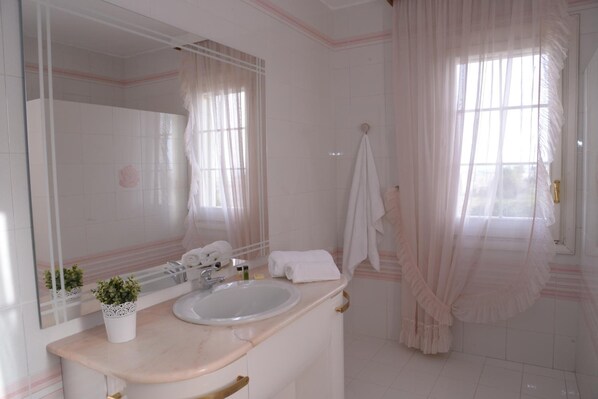 Un baño con lavamanos blanco, espejo y una planta en maceta.