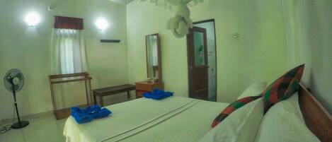 Ein Hotelzimmer mit Bett, Nachttisch, Spiegel und Ventilator.