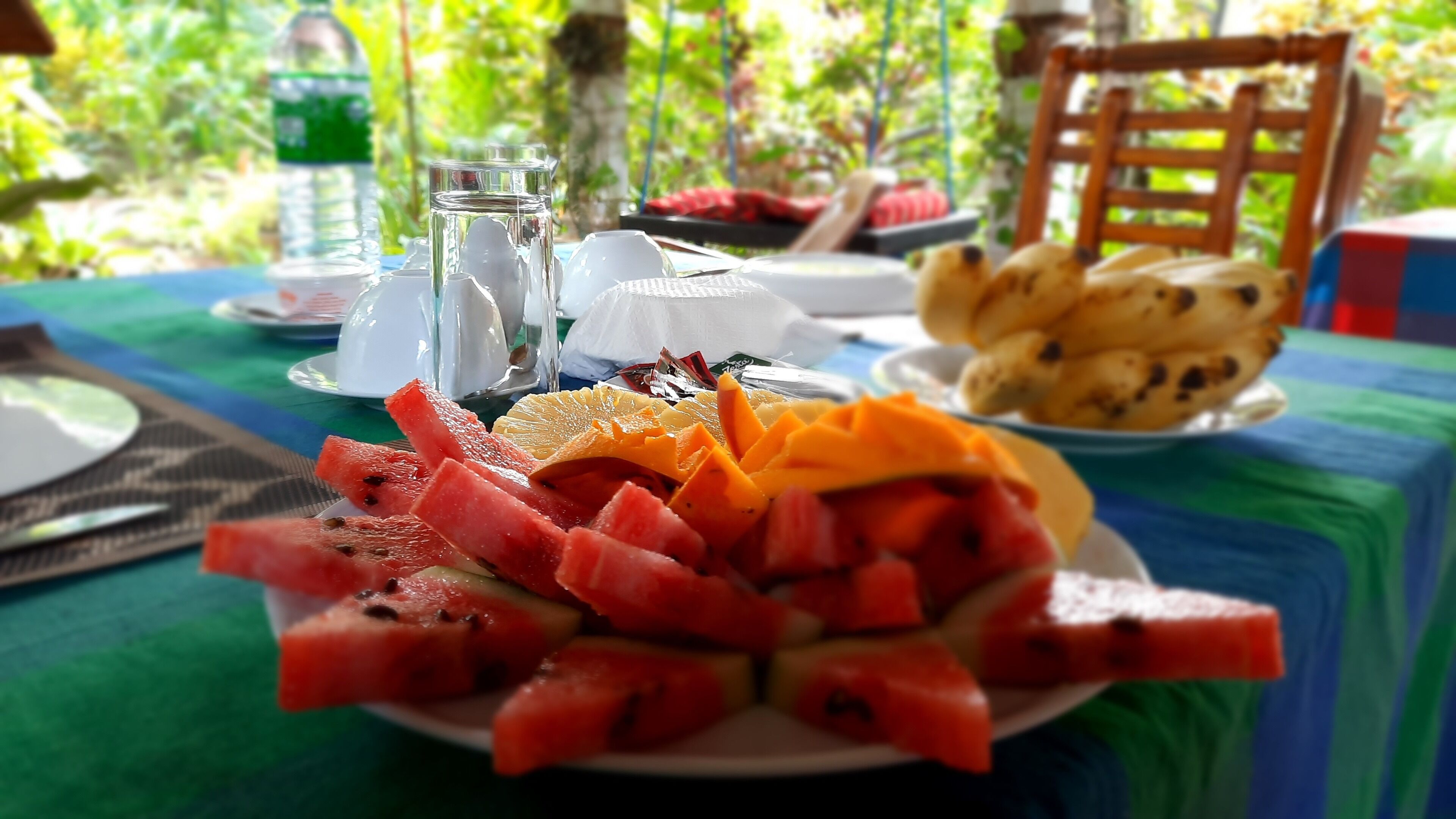 A table with a plate of watermelon and mango slices, a glass of water, and a plate of bread.
