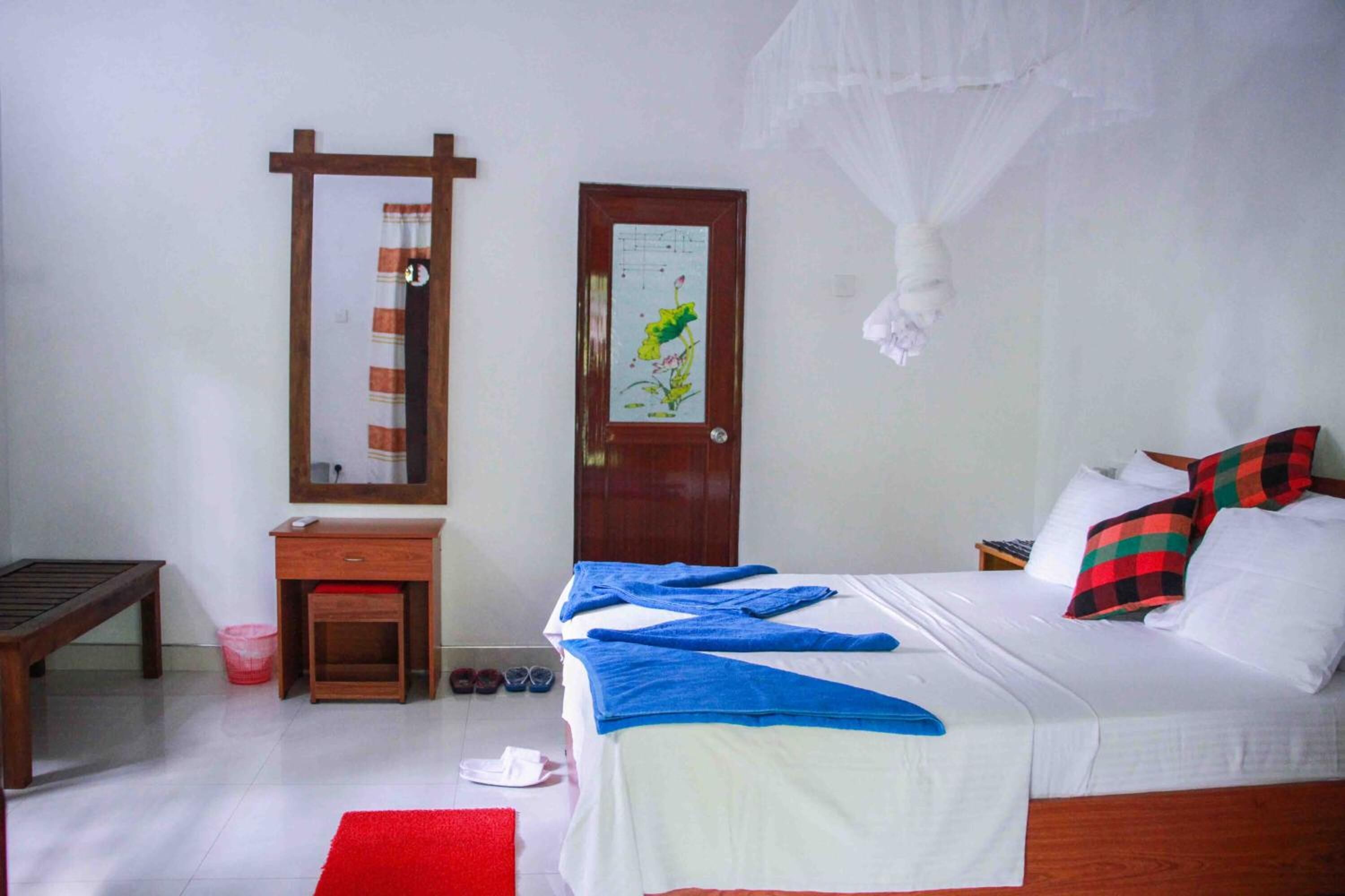 A bedroom with a bed, a bedside table, a mirror, a door with a floral decoration, and a red rug.