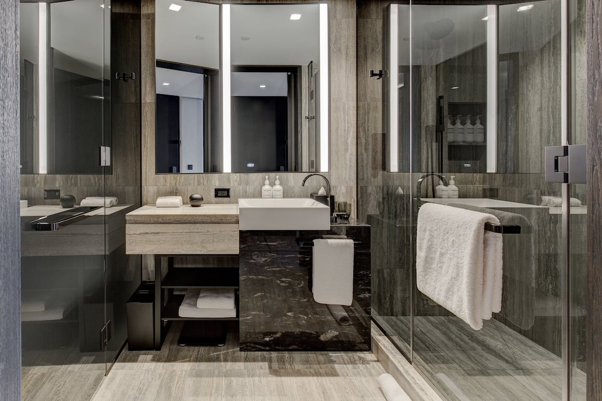 Un bany modern amb dutxa envidriada, un lavabo amb un gran mirall i un paviment de marbre.
