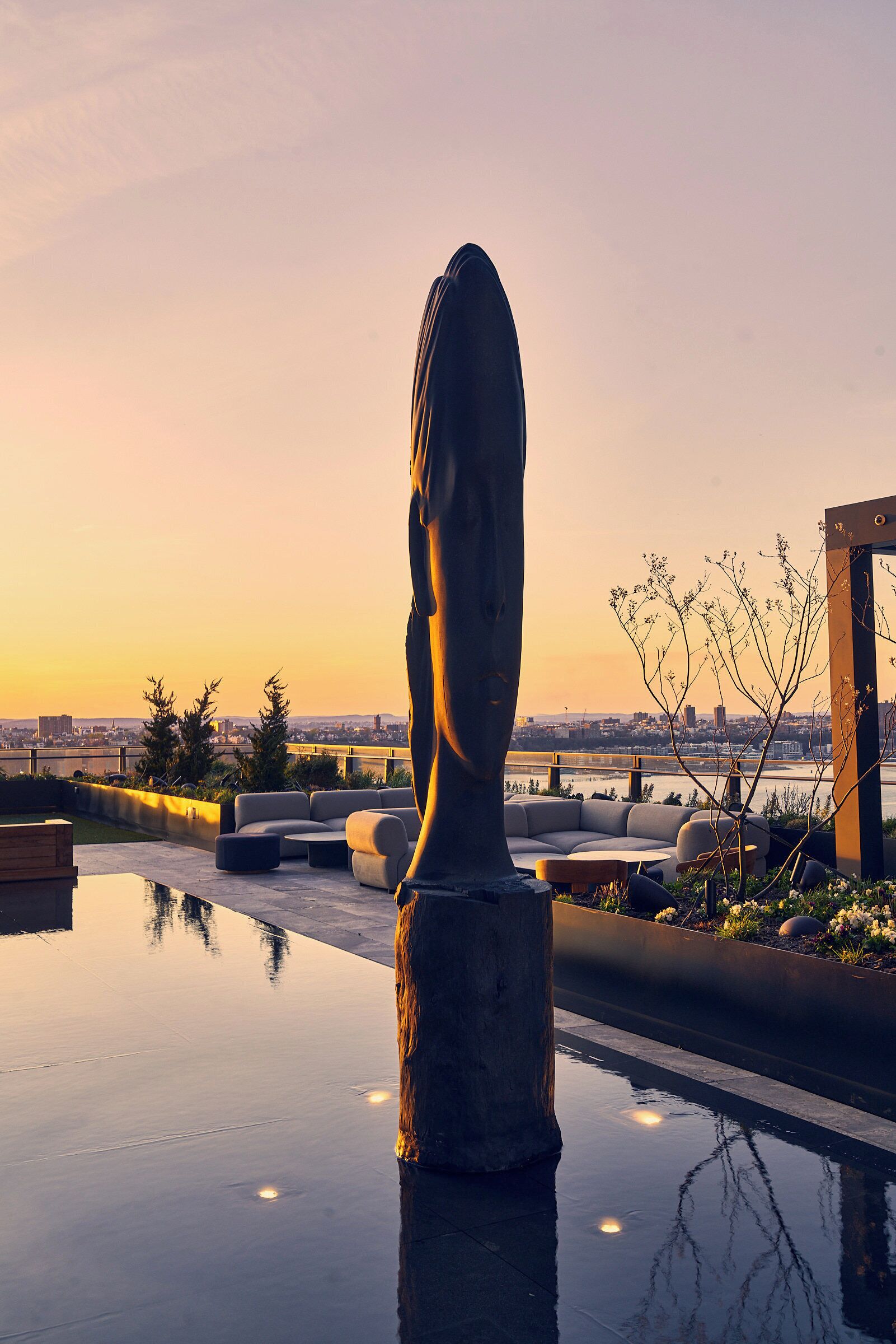 A sculpture on a reflective pool with a city view at sunset.