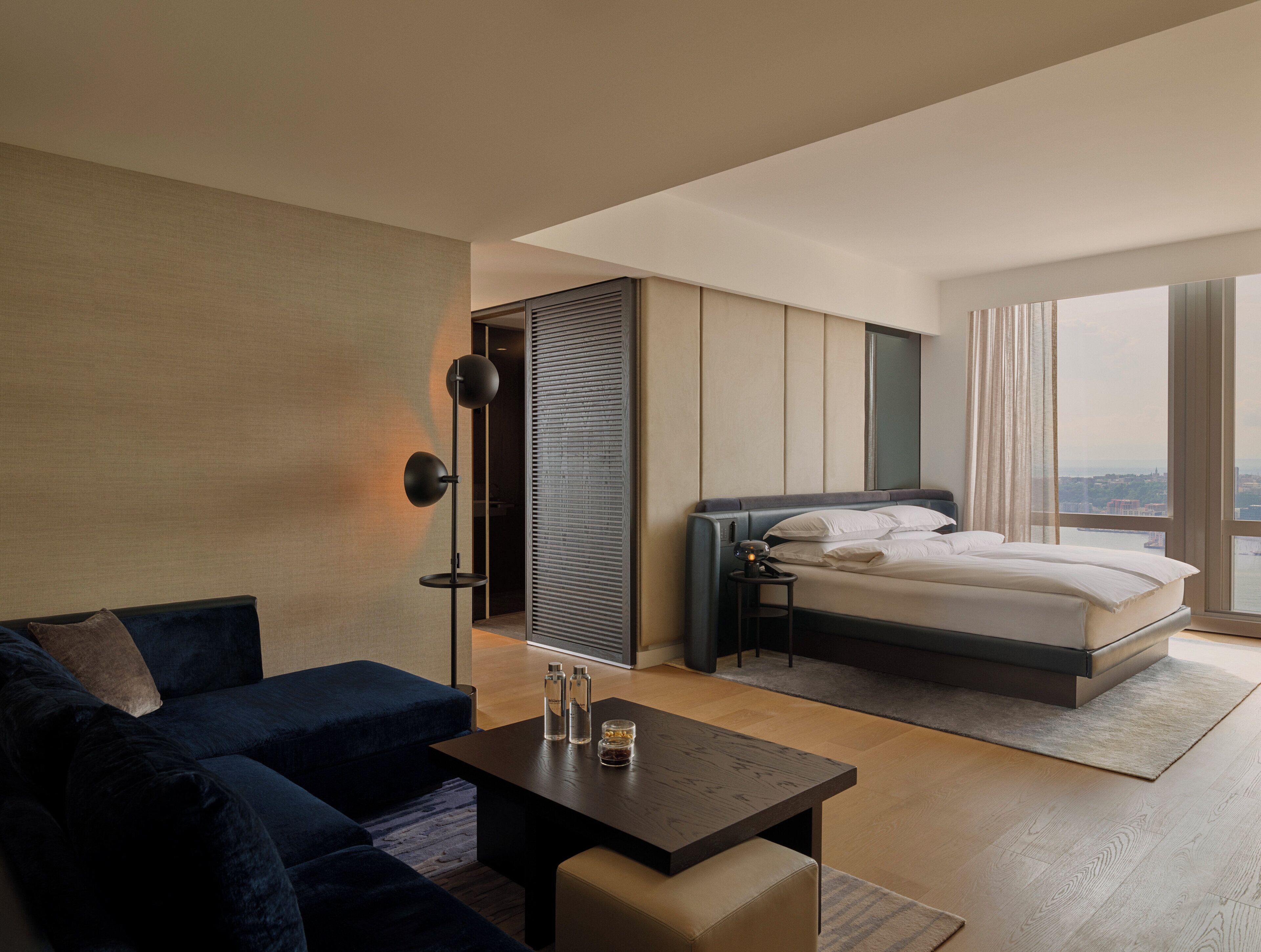 Une chambre d’hôtel moderne, équipée d’un lit, d’un canapé, d’une table basse et offrant une vue sur la ville.