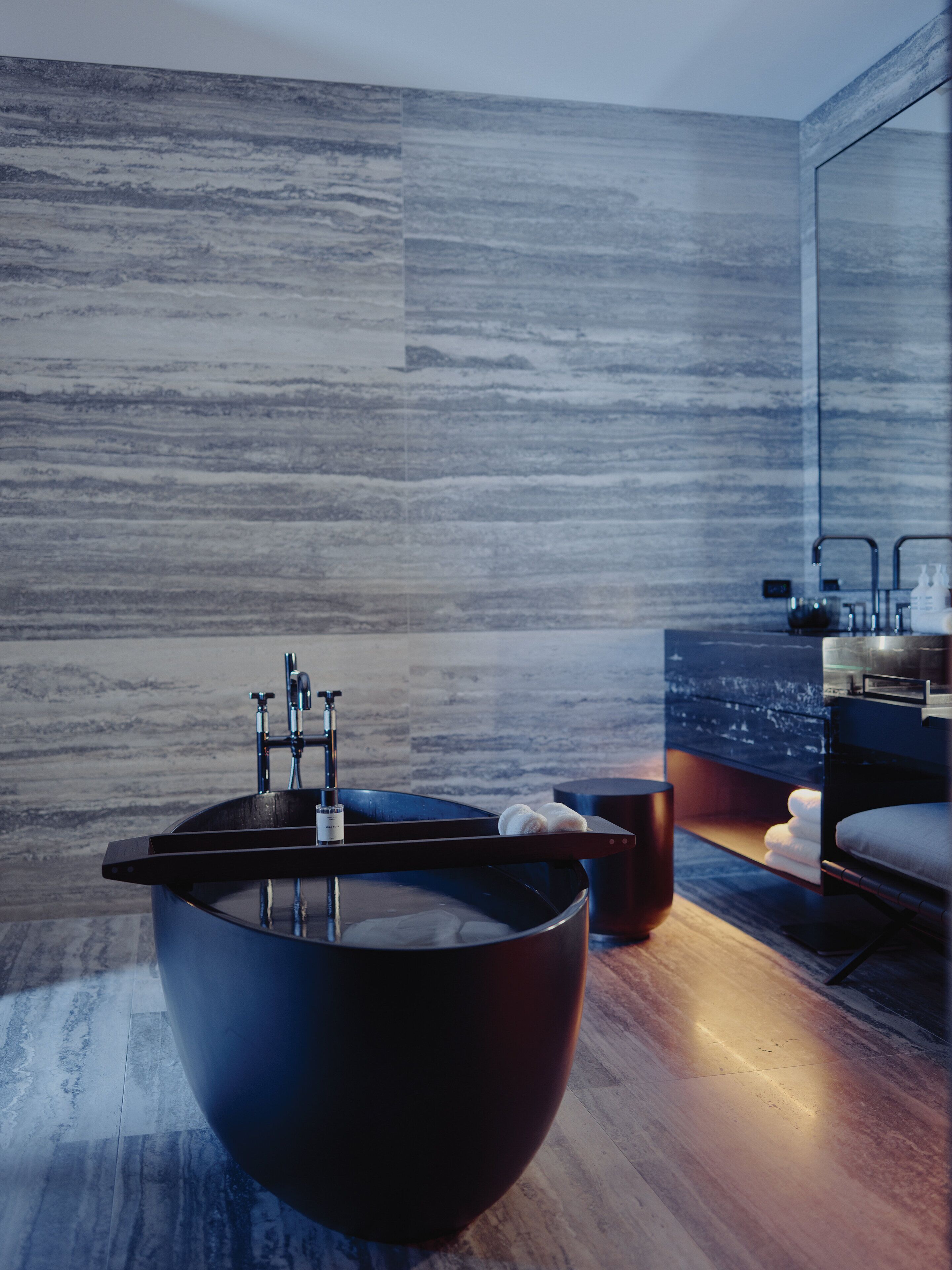 A modern bathroom with a large, dark, bowl-shaped bathtub, a visible faucet, and a wooden floor.