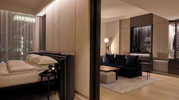 Habitación de hotel moderna con sofá, una mesita, una silla, un espejo y vistas panorámicas de la ciudad a través de amplias ventanas.