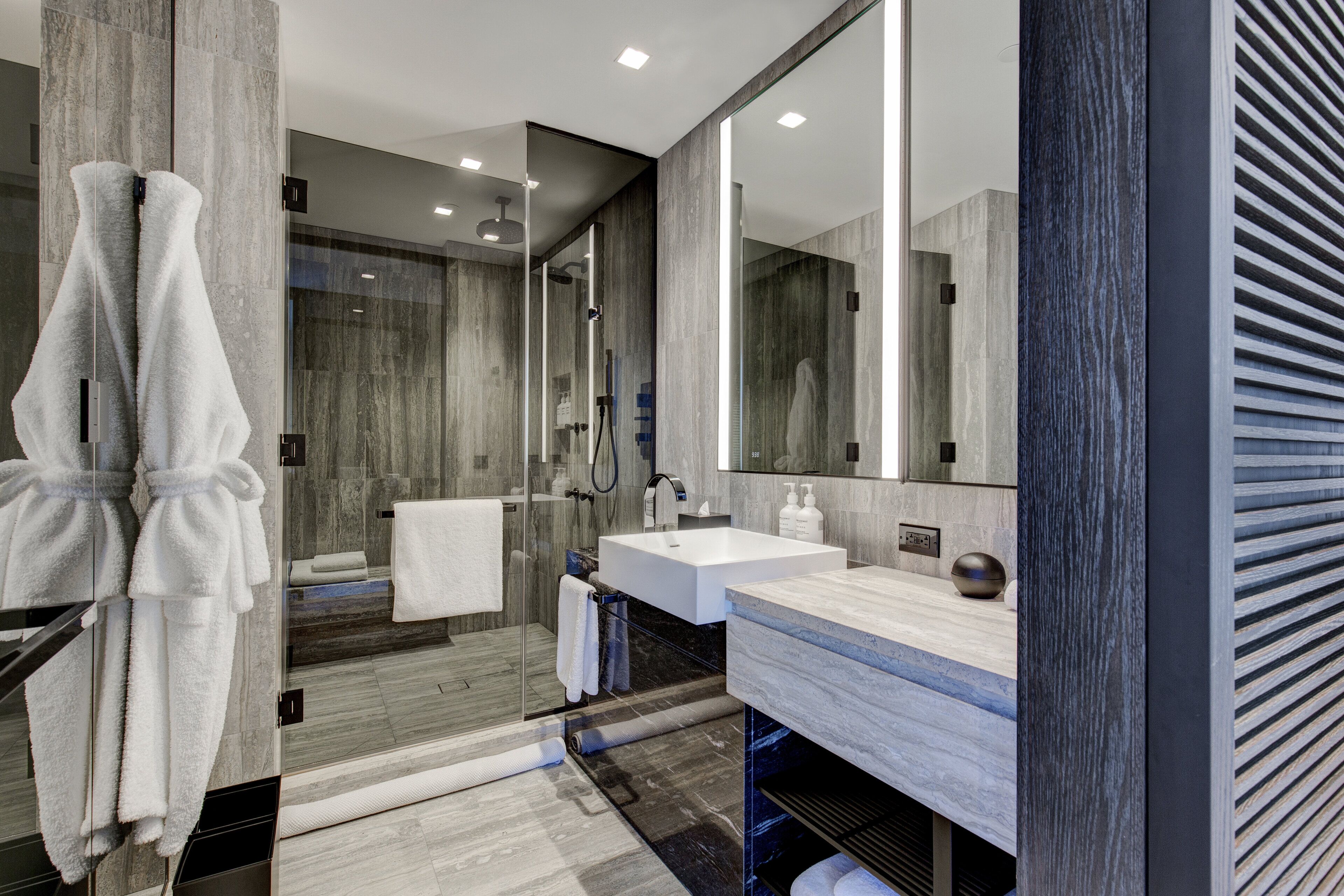 A modern bathroom with a glass shower enclosure, a large mirror, and a marble countertop.