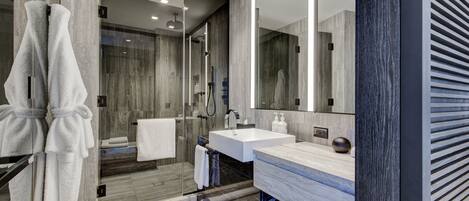 A modern bathroom with a glass shower enclosure, a large mirror, and a marble countertop.