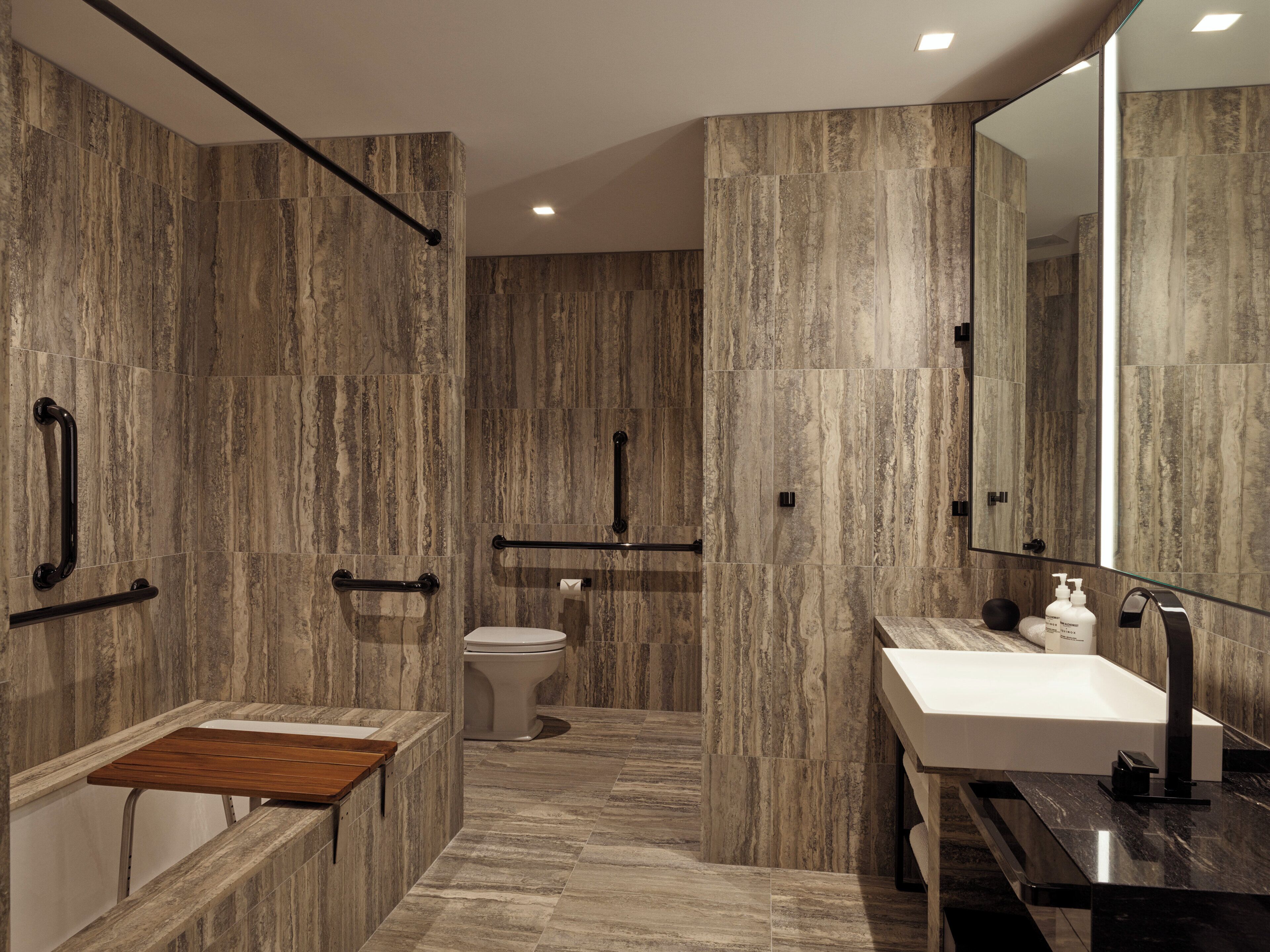 A modern bathroom with a marble floor, a wooden vanity, a white sink, and a large mirror.