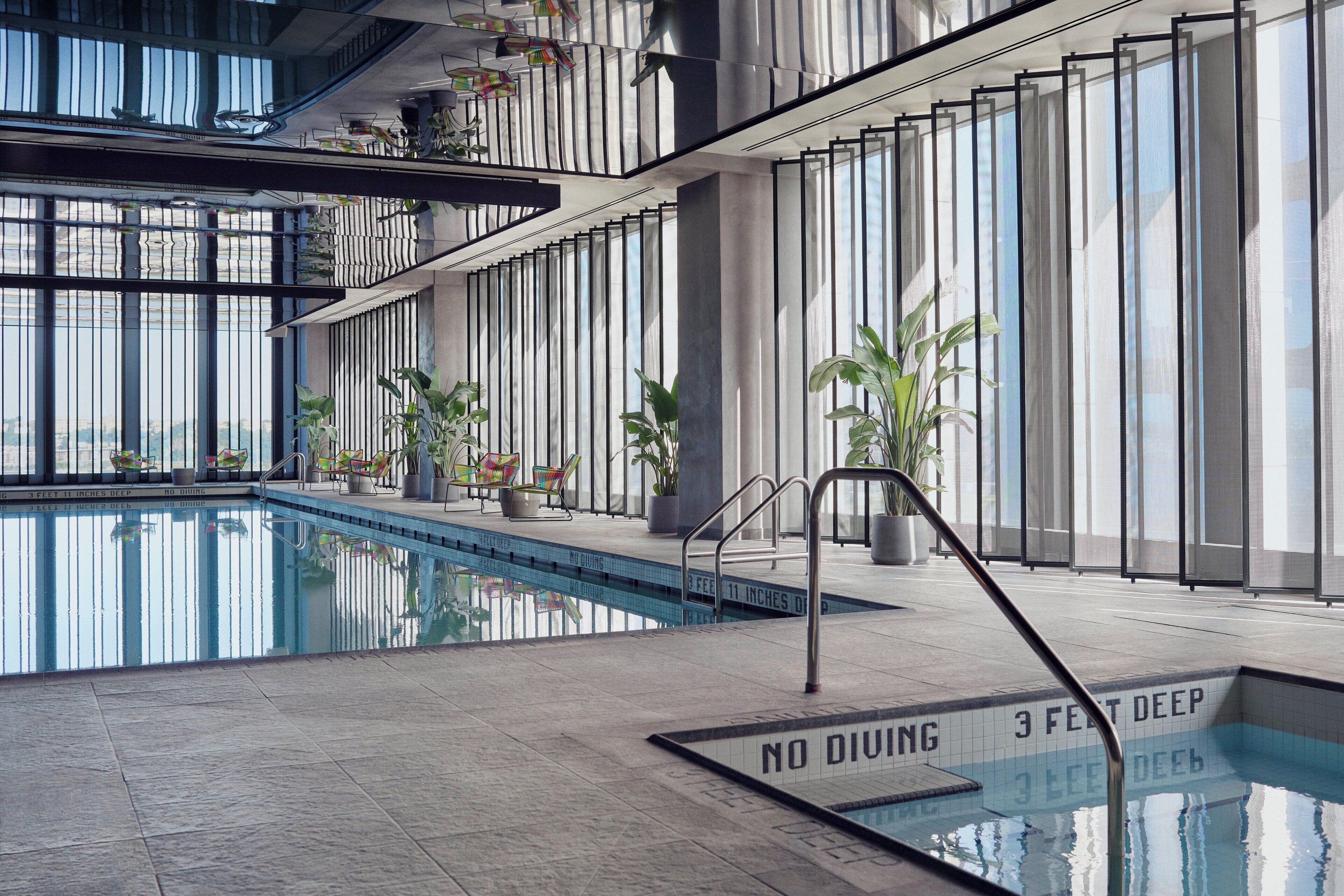 A modern indoor swimming pool with clear water, surrounded by large windows and potted plants.