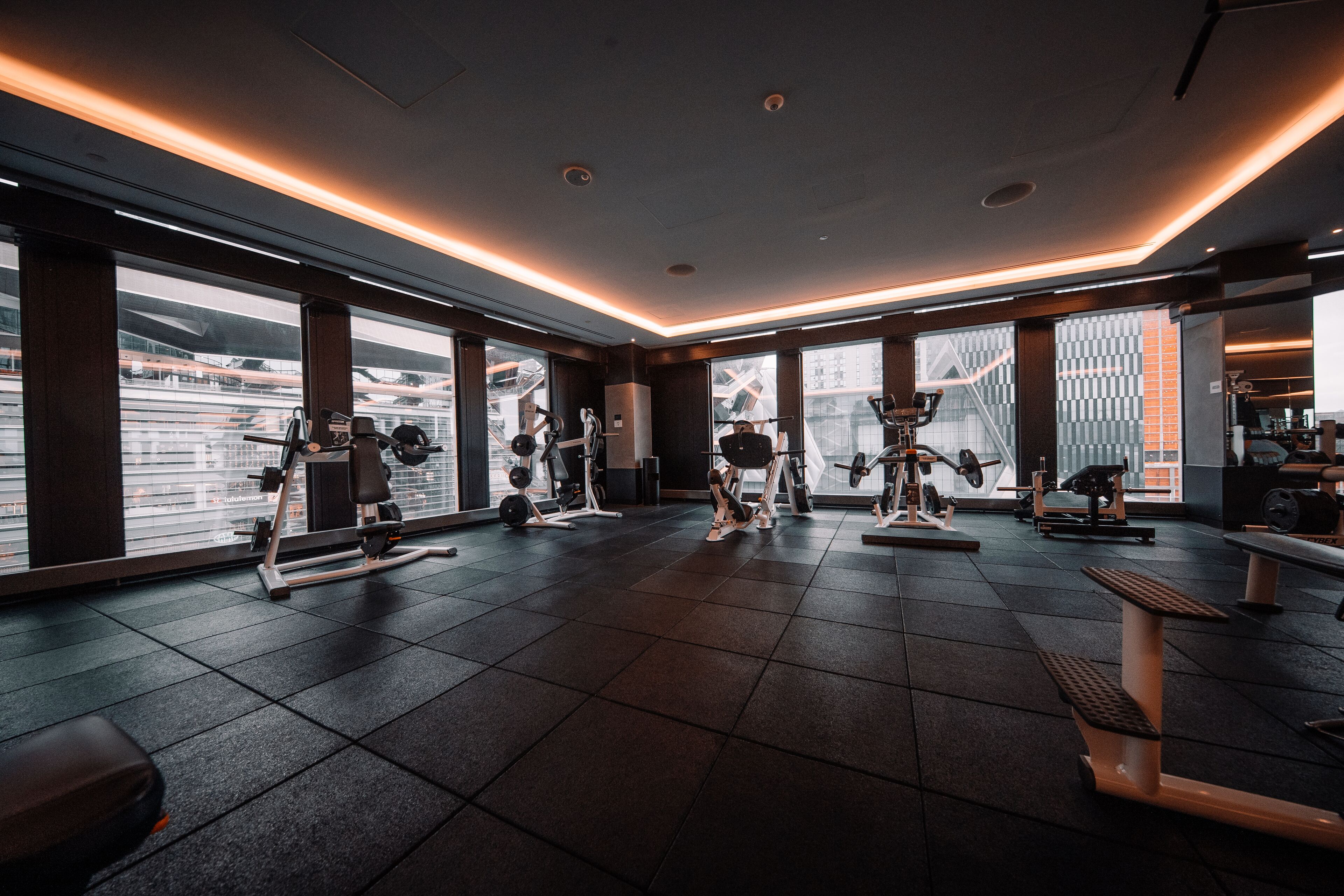 A modern gym with various exercise equipment, large windows, and a clean, tiled floor.