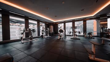A modern gym with various exercise equipment, large windows, and a clean, tiled floor.